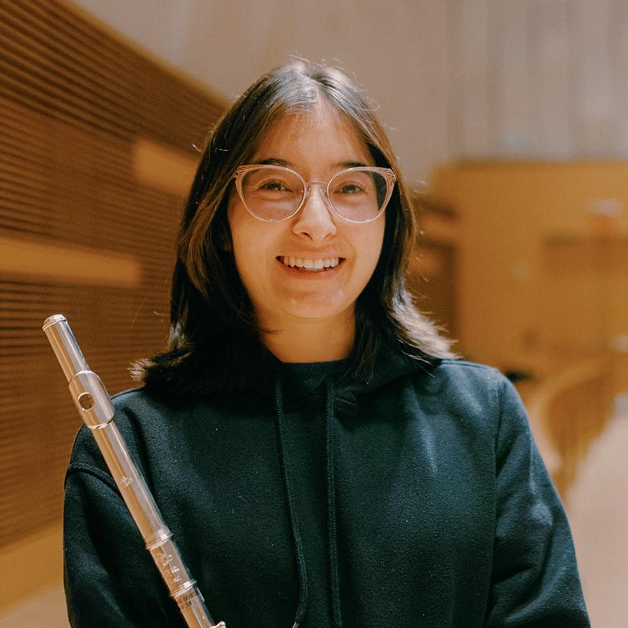 Mya-Jai holds flute smiling in the auditorium.